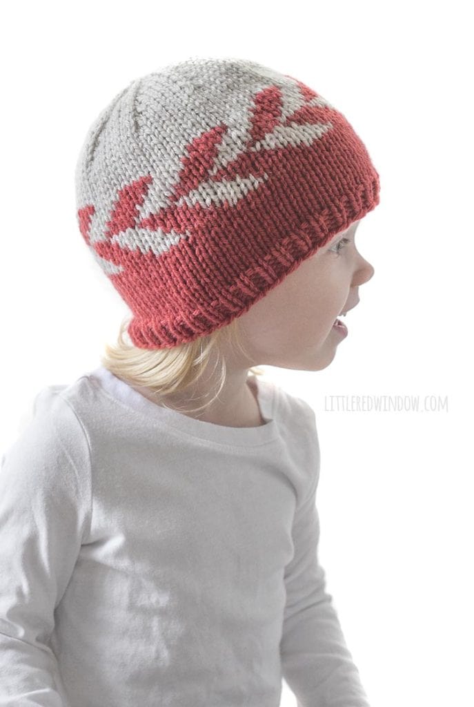 smiling girl in white shirt wearing knit hat with red and tan zipper pattern around the middle looking off to the right